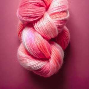 Könnte beinhalten: Eine Knäuel rosa und weißes Garn mit einem Farbverlauf. Das Garn ist weich und flauschig und wäre perfekt zum Stricken oder Häkeln.