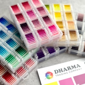 May include: A selection of colourful embroidery floss in clear plastic organisers. The floss is arranged in a gradient of colours, including pinks, blues, greens, and yellows. A colour chart from Dharma Trading Company is also visible.