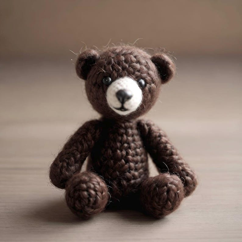 May include: A handmade, crocheted teddy bear in shades of brown. The bear has a white muzzle, black eyes, and a black nose. Its arms and legs are rounded, and it sits upright. The bear is a charming, soft toy.