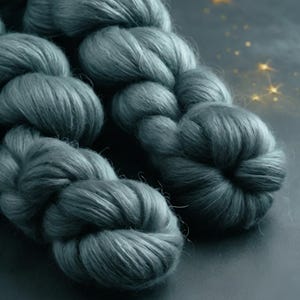 May include: Close-up of a skein of teal-colored yarn. The yarn is thick and fluffy, with a soft, textured appearance. The image is well-lit, highlighting the yarn's color and texture. The yarn is likely used for knitting or crocheting.