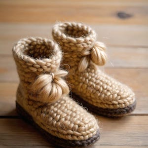 May include: A pair of handmade, beige crochet booties with a dark brown sole and a decorative pom-pom on the side. The chunky knit design suggests warmth and comfort. These cozy slippers are perfect for indoor wear.