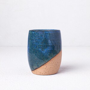 May include: A blue and brown ceramic mug with a speckled glaze. The mug is made of stoneware and has a rounded shape.