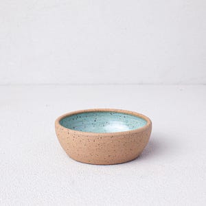 May include: A small, speckled, light brown ceramic bowl with a light blue glaze inside.
