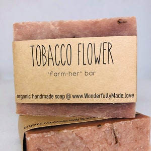 May include: Two bars of handmade soap wrapped in brown paper. The top bar has a label that reads "TOBACCO FLOWER "farm-her" bar" and "organic handmade soap @ www.WonderfullyMade.love".