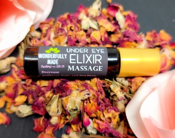 May include: A small amber glass roller bottle with a black label that reads "Under Eye Elixir Massage" and "Wonderfully Made". The bottle is surrounded by rose petals.