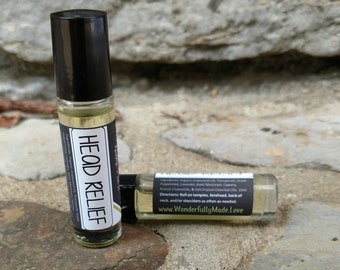 May include: Two small glass bottles with black roll-on tops and labels. The front label says "HEAD RELIEF" and the back label lists ingredients and directions. The bottles are sitting on a rocky surface.