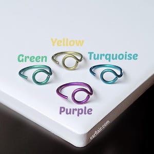 May include: Four colorful nose rings in green, yellow, turquoise, and purple. Each ring has a curved design with a circular accent. The rings are displayed on a white surface with the text "Green", "Yellow", "Turquoise", and "Purple". The website "earflair.com" is also visible.