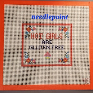 May include: Needlepoint canvas with the text "HOT GIRLS ARE GLUTEN FREE" in red, cross-stitched lettering. The canvas has an orange border and is decorated with floral cross-stitch designs. The word "needlepoint" is written in blue.