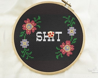 Puede incluir: Un aro de bordado negro con un diseño floral alrededor de los bordes. La palabra "SHIT" está bordada en blanco con un pequeño grupo de setas rojas en el centro de la palabra.