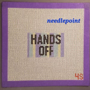 May include: A needlepoint canvas with a purple border and a white mesh background. The words "HANDS OFF" are stitched in black block letters. The word "needlepoint" is written in blue cursive. The number "45" is in the bottom right corner.