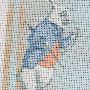 Peut inclure: Lapin blanc portant une veste bleue et un gilet orange, tenant une montre de poche et une canne. Le lapin est repr&eacute;sent&eacute; dans un style point de croix.