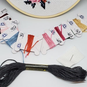 Puede incluir: Surtido de carretes de hilo de bordar DMC en varios colores, incluyendo rojo, rosa, azul, verde y marr&oacute;n. Los carretes est&aacute;n etiquetados con los n&uacute;meros DMC. Tambi&eacute;n se incluye un peque&ntilde;o trozo de tela Aida blanca con una aguja.