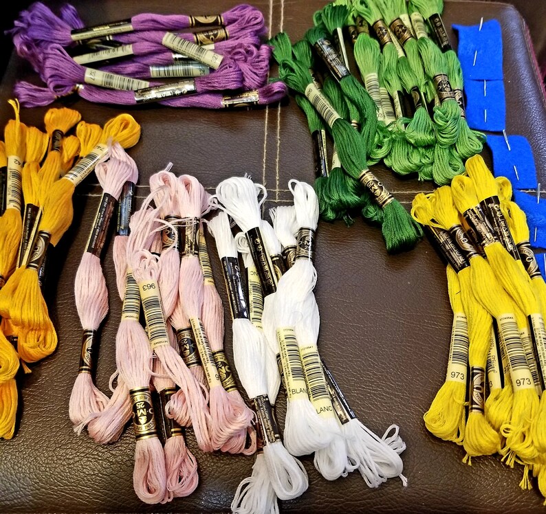 May include: Assortment of embroidery floss spools in various colors, including purple, green, white, pink, and yellow. The spools are labeled with numbers and the words "Blanc" and "Land".