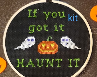 May include: A black embroidery hoop with a white background and green text that reads "If you got it HAUNT IT". There is a white ghost on each side of an orange pumpkin with a smiling face.