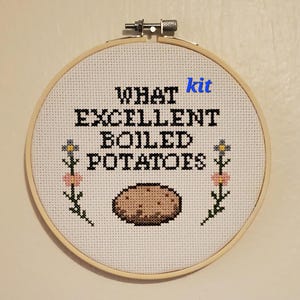 May include: Cross-stitch embroidery in a wooden hoop. The design features the text "WHAT EXCELLENT BOILED POTATOES" with a potato illustration and floral accents. The word "kit" is in blue.