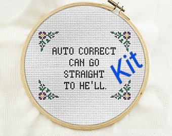 May include: A cross-stitch project in a round wooden hoop featuring the black text AUTO CORRECT CAN GO STRAIGHT TO HE'LL. The design includes small floral corner accents in purple and green on white Aida cloth, with the blue word Kit.