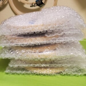 May include: A stack of four round wooden embroidery hoops wrapped in bubble wrap, ready for shipping.