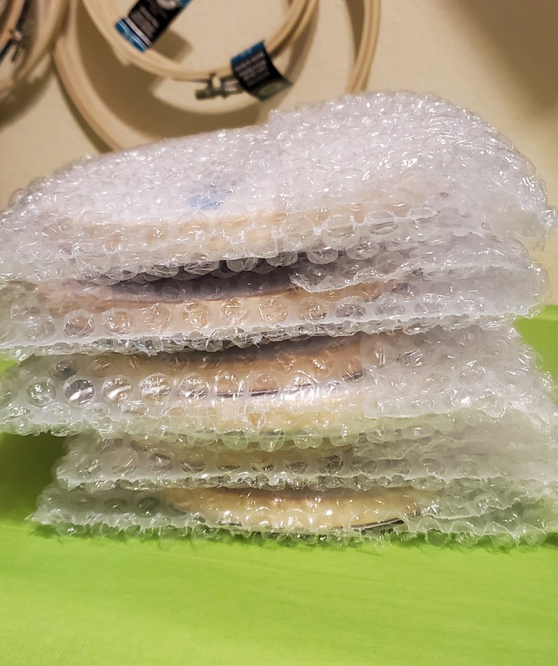 May include: A stack of four round wooden embroidery hoops wrapped in bubble wrap, ready for shipping.