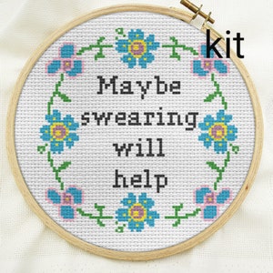 Puede incluir: Kit de punto de cruz en un aro de madera con el texto "Maybe swearing will help". El diseño presenta un borde floral con flores azules y rosas y vides verdes sobre un fondo blanco. La palabra "kit" está en la esquina superior derecha.