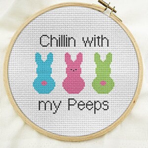 Peut inclure: Un cercle de broderie blanc avec le texte "Chillin' with my Peeps" et trois figures de lapin de couleur. Les lapins sont bleus, roses et verts.