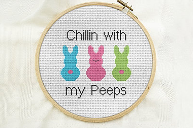 Peut inclure: Un cercle de broderie blanc avec le texte "Chillin' with my Peeps" et trois figures de lapin de couleur. Les lapins sont bleus, roses et verts.