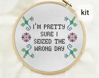Puede incluir: Kit de bordado de punto de cruz con un aro blanco sobre un fondo blanco y el texto "I'm pretty sure I seized the wrong day" en negro. El aro está rodeado por un marco de madera y decorado con pequeñas flores azules y verdes.