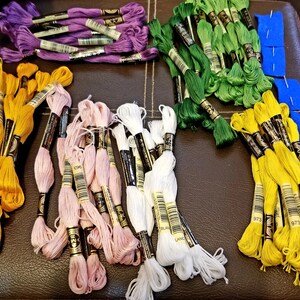 Peut inclure: Assortiment de bobines de fil &agrave; broder de diff&eacute;rentes couleurs, dont le violet, le vert, le jaune, le rose et le blanc. Les bobines sont &eacute;tiquet&eacute;es avec des num&eacute;ros et les mots "Blanc" et "Land".