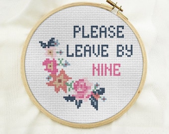 Puede incluir: Un aro de bordado blanco con un diseño de punto de cruz que dice "PLEASE LEAVE BY NINE" en letras negras y rosas. El diseño está rodeado por un borde floral con flores rosas, naranjas y azules.