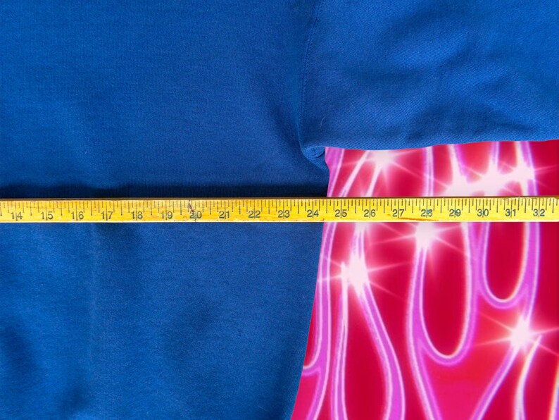 May include: A close-up of a blue sweatshirt with a yellow measuring tape across the bottom. The tape measures 14 to 32 inches.
