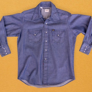May include: A blue denim long-sleeve shirt with a button-down collar, two chest pockets, and a Lee brand label. The shirt has a classic Western style.