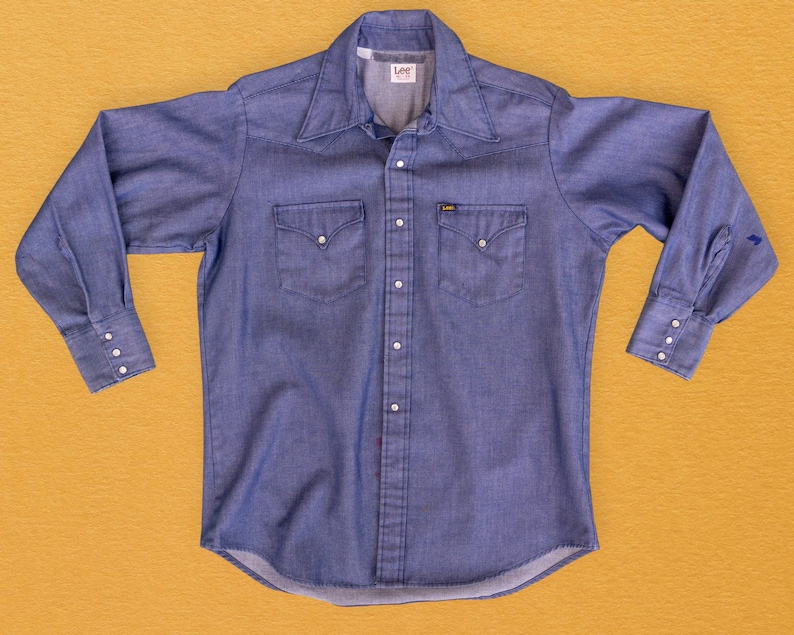 May include: A blue denim long-sleeve shirt with a button-down collar, two chest pockets, and a Lee brand label. The shirt has a classic Western style.
