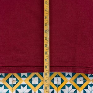 May include: A close-up of a burgundy t-shirt with a wooden ruler measuring 28 inches. The t-shirt is laying on a tiled surface.
