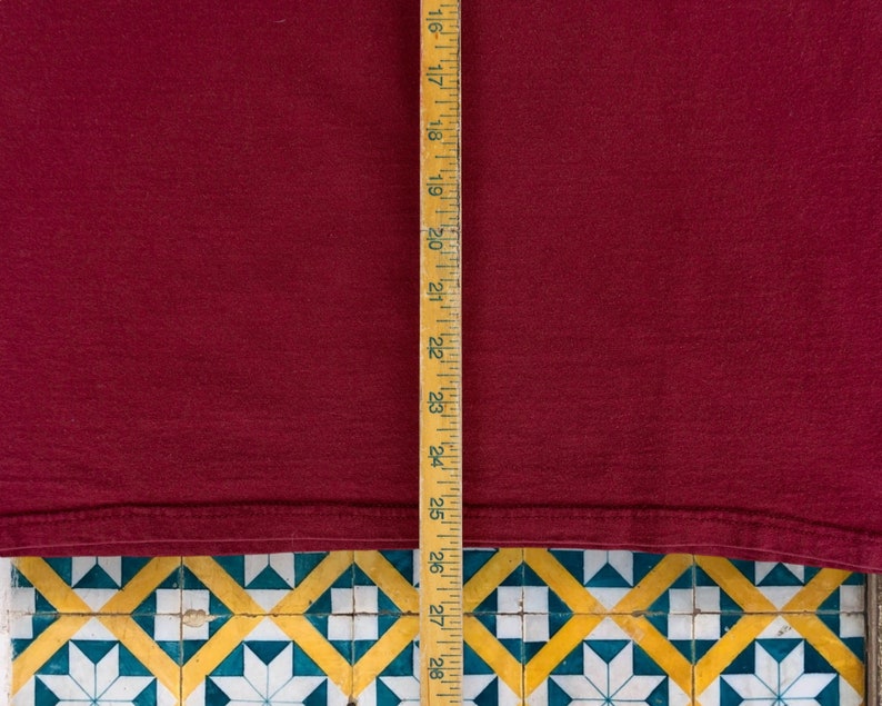 May include: A close-up of a burgundy t-shirt with a wooden ruler measuring 28 inches. The t-shirt is laying on a tiled surface.