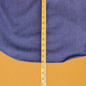 May include: A close-up of a blue denim fabric with a wooden ruler measuring 34 inches. The fabric is a solid blue color and has a slight texture.
