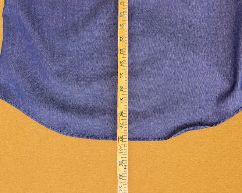 May include: A close-up of a blue denim fabric with a wooden ruler measuring 34 inches. The fabric is a solid blue color and has a slight texture.