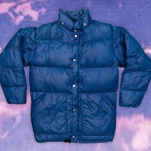 Peut inclure: Veste bouffante bleue avec un col montant et des fermetures à boutons-pression. La veste présente un design matelassé et deux poches avant. Les manches sont longues et la veste est faite d'un matériau brillant. L'arrière-plan est un mélange flou de violet et de bleu.