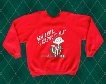 Può includere: Felpa rossa di Natale con un personaggio dei cartoni animati e il testo "Caro Babbo Natale, "Me lo merito tutto!"