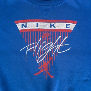 May include: A blue sweatshirt with a red, white, and blue Nike logo and the word "Flight" in white lettering. The logo is in the shape of a triangle with red and white stripes.