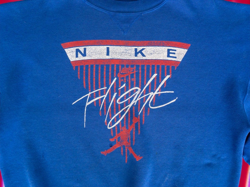 May include: A blue sweatshirt with a red, white, and blue Nike logo and the word "Flight" in white lettering. The logo is in the shape of a triangle with red and white stripes.