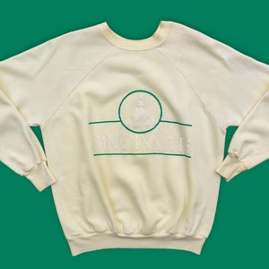 May include: A vintage cream-colored sweatshirt with a green and white embroidered logo that says "Cincinnati".