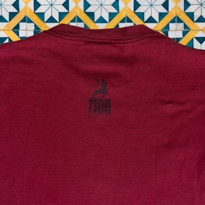 May include: A maroon t-shirt with a black graphic of a person holding a microphone and the text "Zion Collective" on the back.
