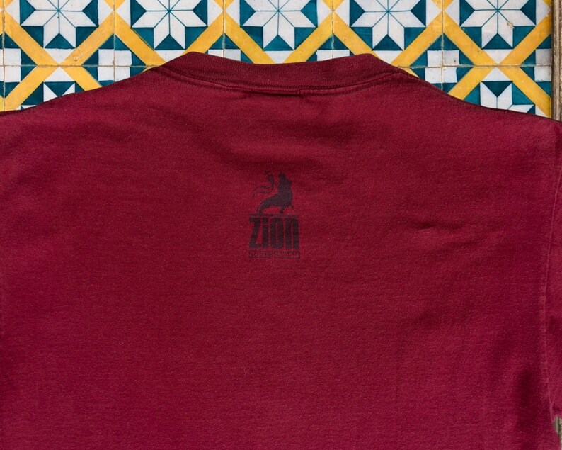 May include: A maroon t-shirt with a black graphic of a person holding a microphone and the text "Zion Collective" on the back.