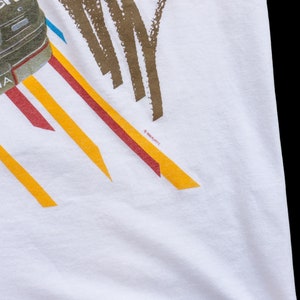 May include: White t-shirt with a graphic of a black car with the word "LUMINA" on the side. The car is surrounded by colorful stripes and the text "&copy;1991 GM/ITC" is visible in the bottom right corner.