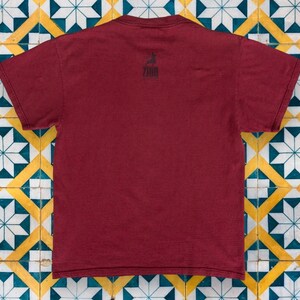 May include: A maroon t-shirt with a black graphic of a person surfing on a wave. The graphic includes the word "ZOO" in black text.