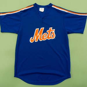 Op de afbeelding: Een blauw baseballshirt met oranje en witte bies. Het shirt heeft het woord "Mets" in oranje letters op de voorkant.