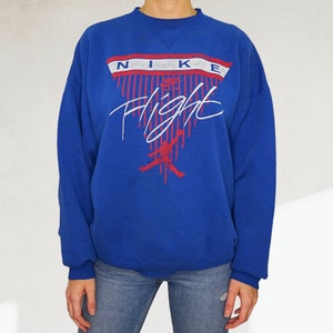 May include: A royal blue sweatshirt with a white and red Nike Flight graphic. The graphic features a basketball player in silhouette and the word "Nike" in a white and red banner.