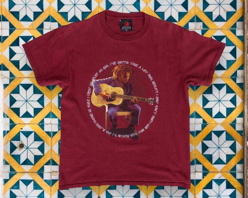 May include: A maroon t-shirt with a graphic print of a man playing a guitar. The text around the image reads "I've gotta take a lot of red, really I don't want to be dancing, why I'm staying with the rest of you".