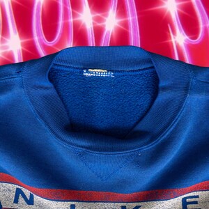 May include: A blue sweatshirt with a white and red logo that says "NIKE" on the front. The sweatshirt has a crew neck and is made of a soft, comfortable material.