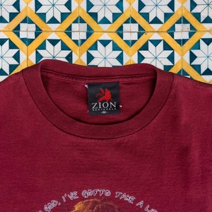 May include: A maroon t-shirt with the text "Oh God, I've gotta take a li..." and a small black tag with the text "Zion Rootswear - M."