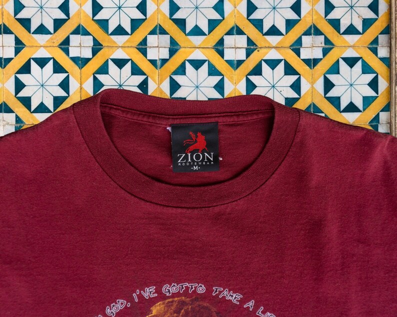 May include: A maroon t-shirt with the text "Oh God, I've gotta take a li..." and a small black tag with the text "Zion Rootswear - M."